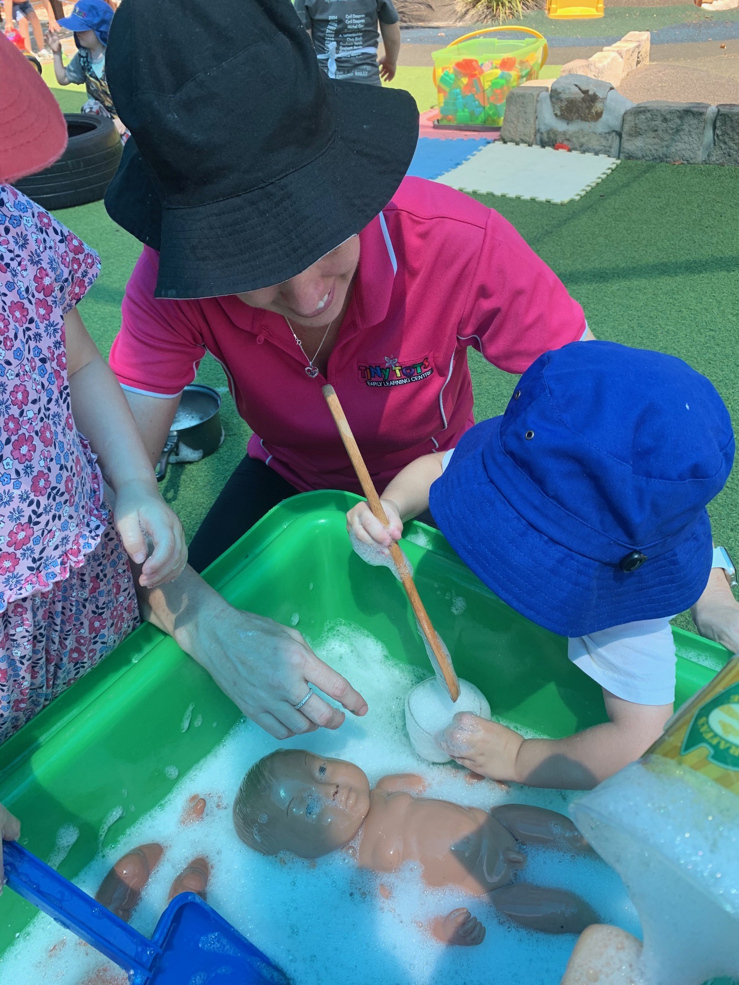 kid washing a doll assisted by a teacher in Tiny Tots Early Learning Centre