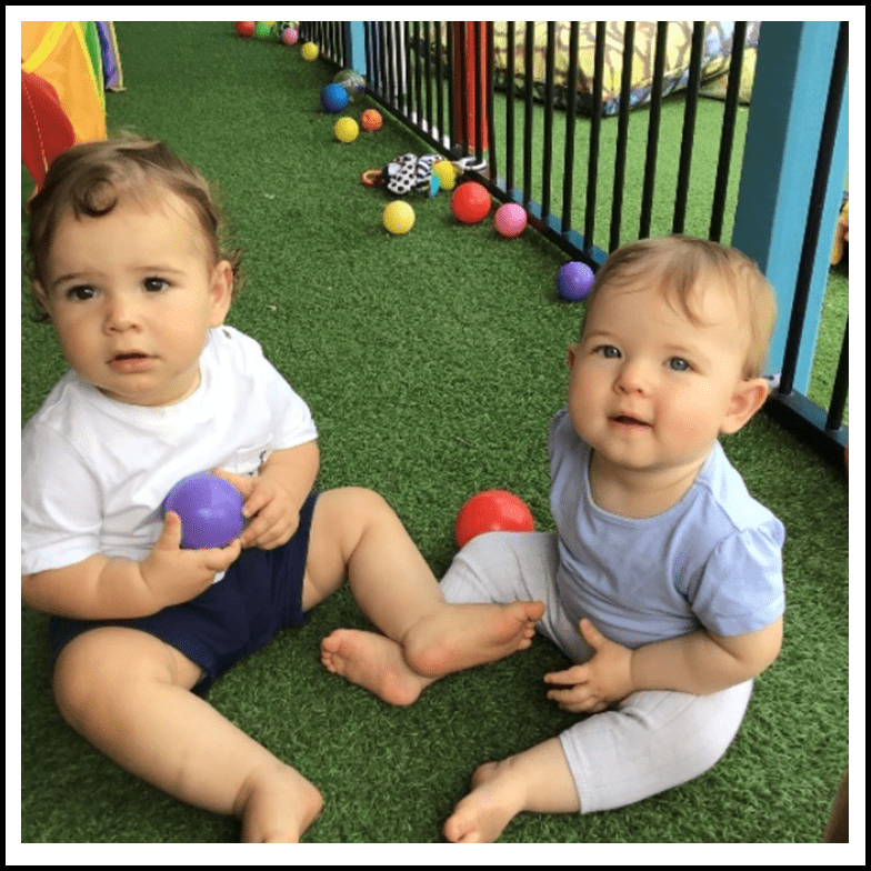 two toddlers sitting on the artificial grass in the play room